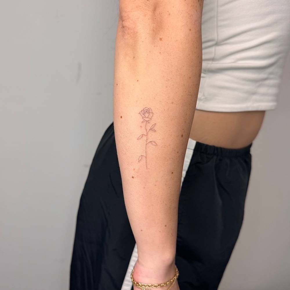Single needle rose tattoo in fine line style placed on the forearm.