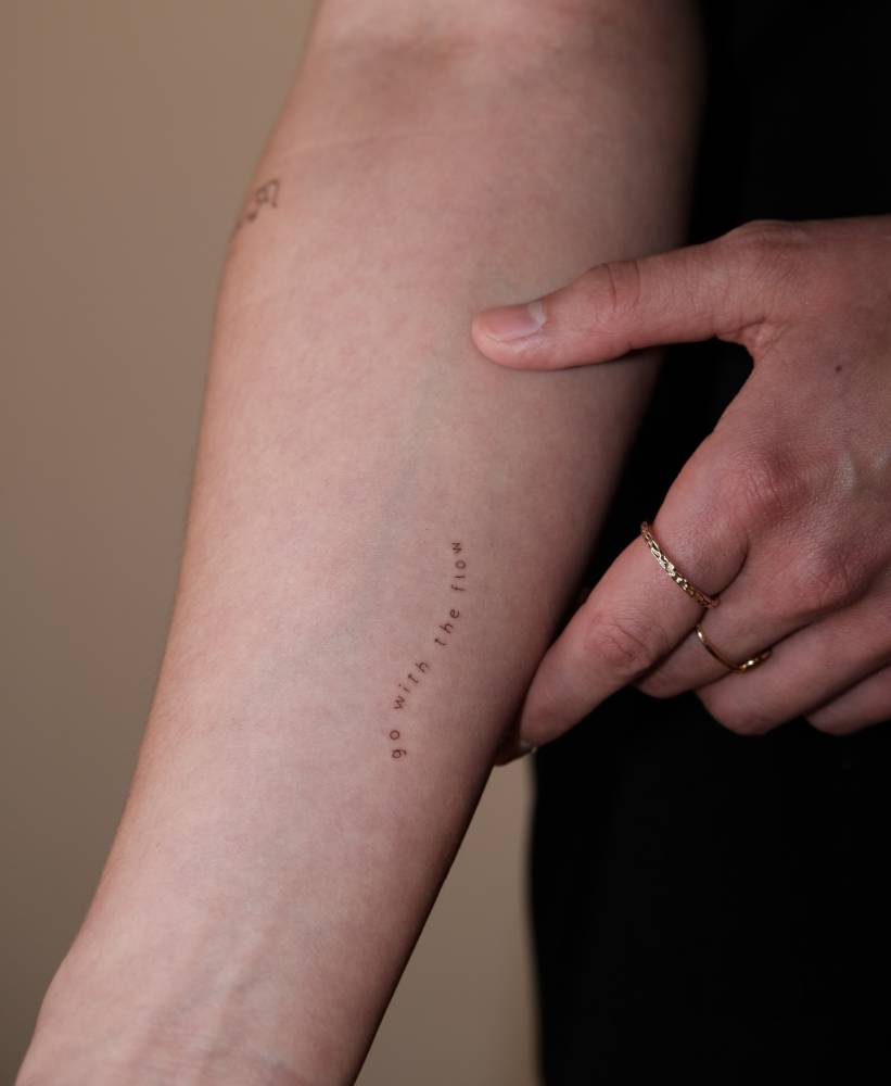 "Go with the flow" lettering tattoo located on the inner forearm.