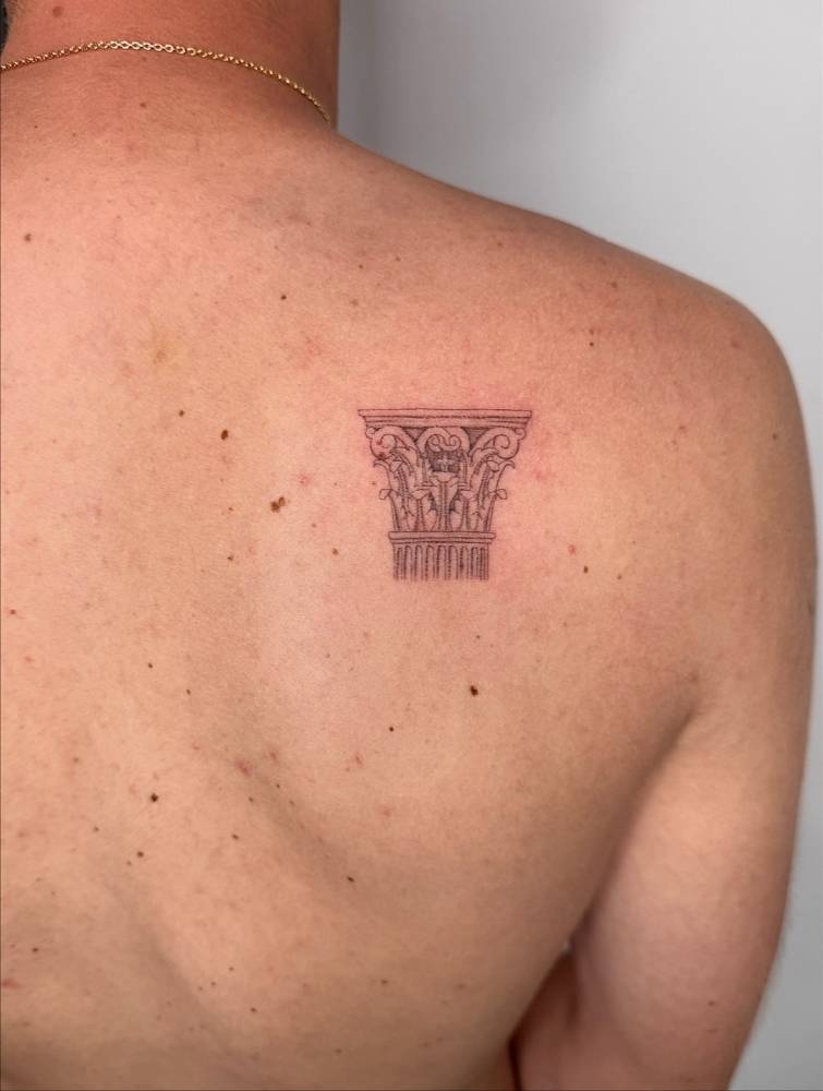 Column tattoo in fine line style placed on the shoulder blade.