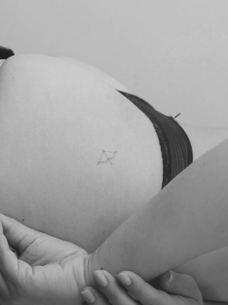 Tiny single needle bow and arrow tattoo located on the butt cheek.