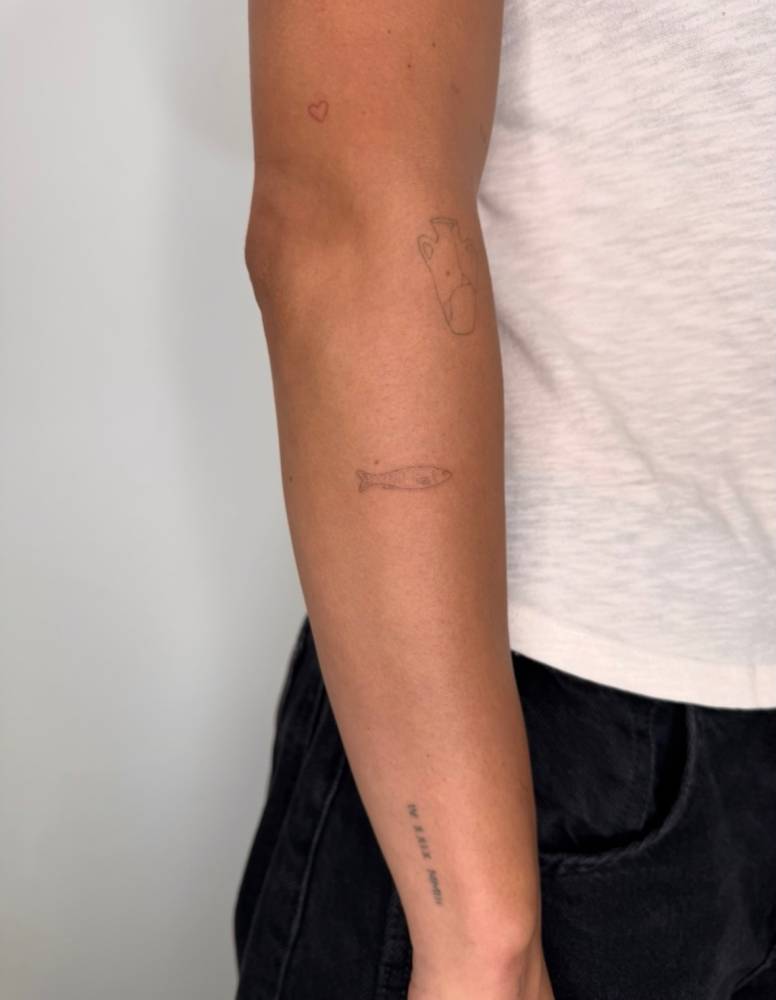 Little fish tattoo in fine line style located on the forearm.