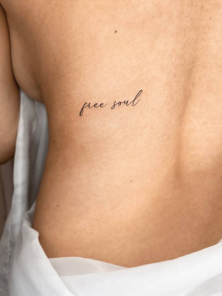 Script font "free soul" lettering tattoo located on the back.