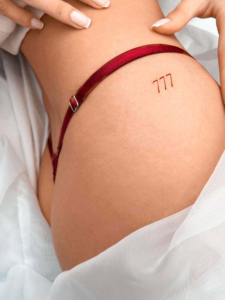 Angel number "777" in red ink tattooed on the hip.