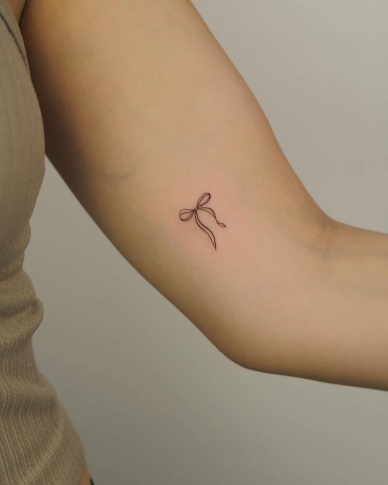 Minimalistic style bow tattoo located on the inner arm.