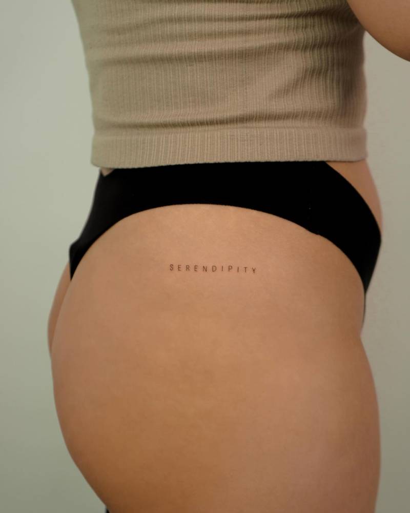 Lettering tattoo of the word "serendipity" located on the hip.