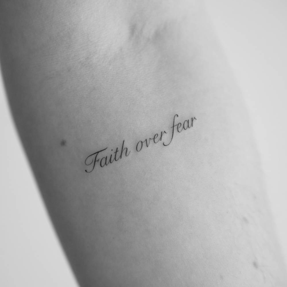 Script font "faith over fear" lettering tattoo done on the inner forearm.