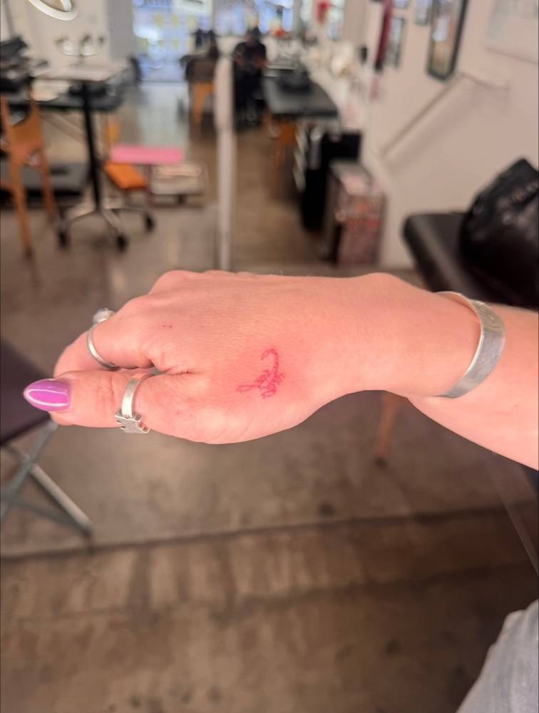 Single needle red scorpion tattoo located on the hand.