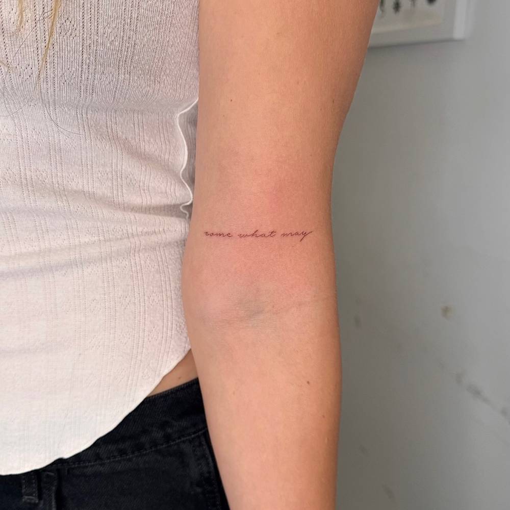 "Come what may" lettering tattoo located on the bicep.