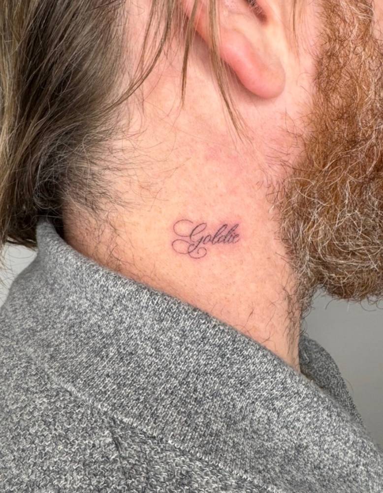 Script font "Goldie" lettering tattoo located on the neck.