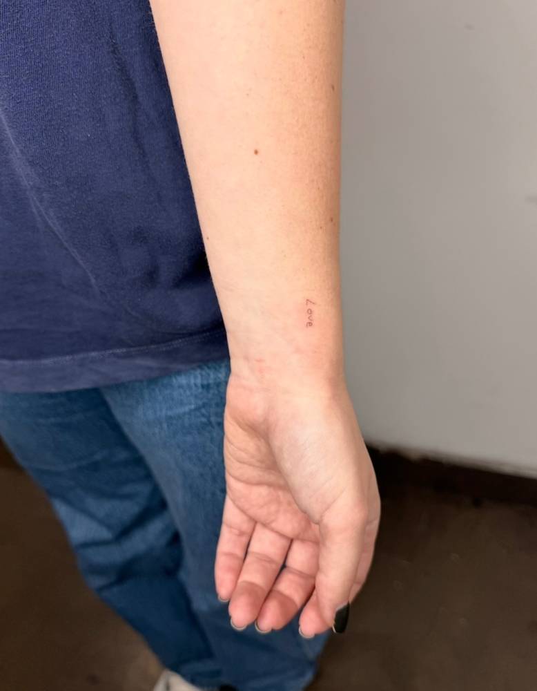 Tiny lettering tattoo of the word "love" placed on the wrist.