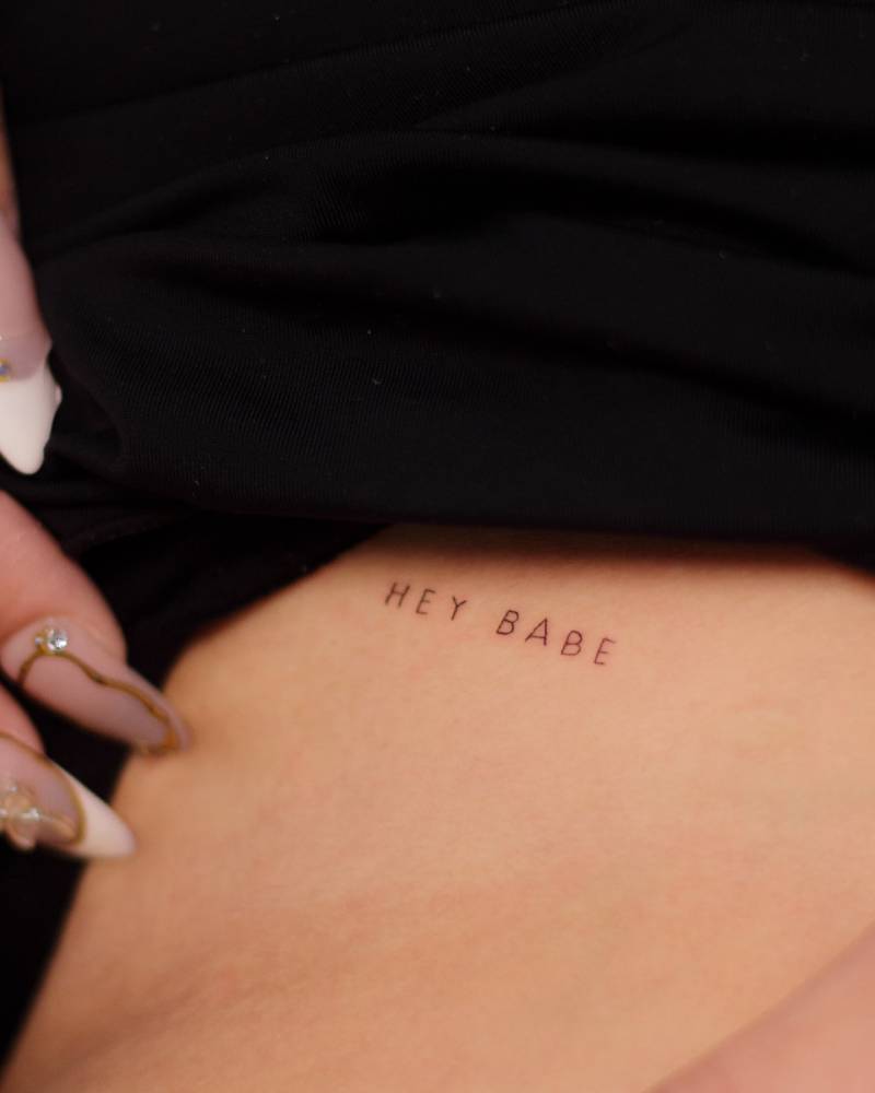 "Hey babe" lettering tattoo located on the pelvis.