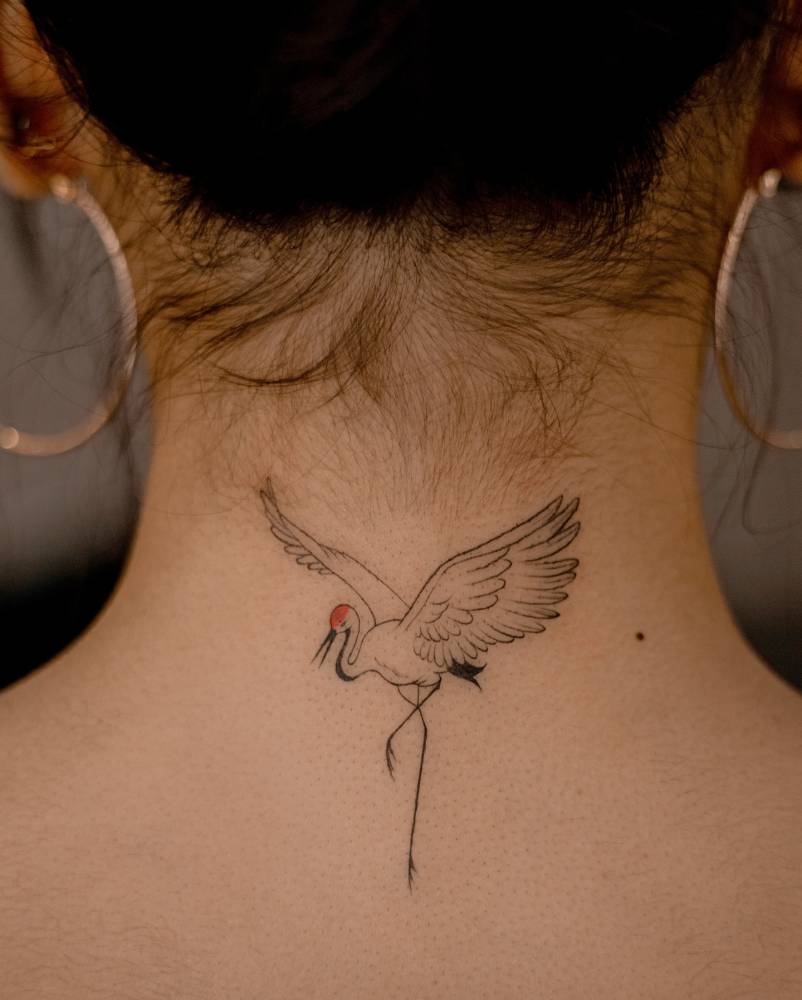 Red crowned crane tattoo in illustrative style located on the back of the neck.