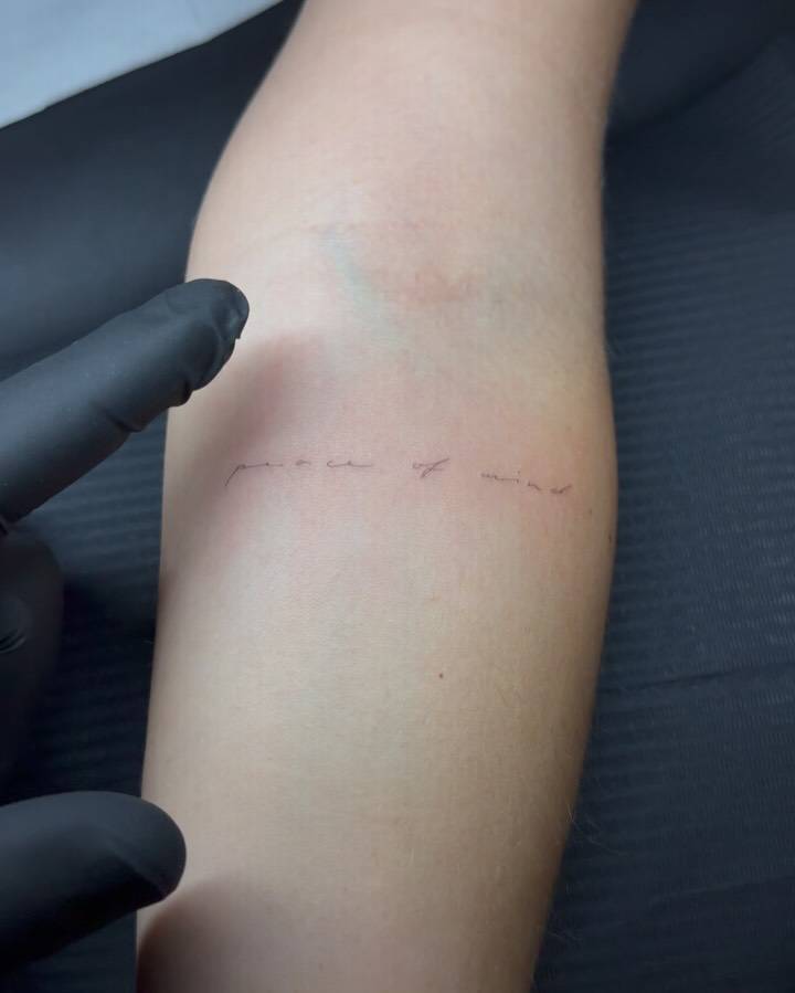 Handwritten font "peace of mind" lettering tattoo done on the inner forearm.