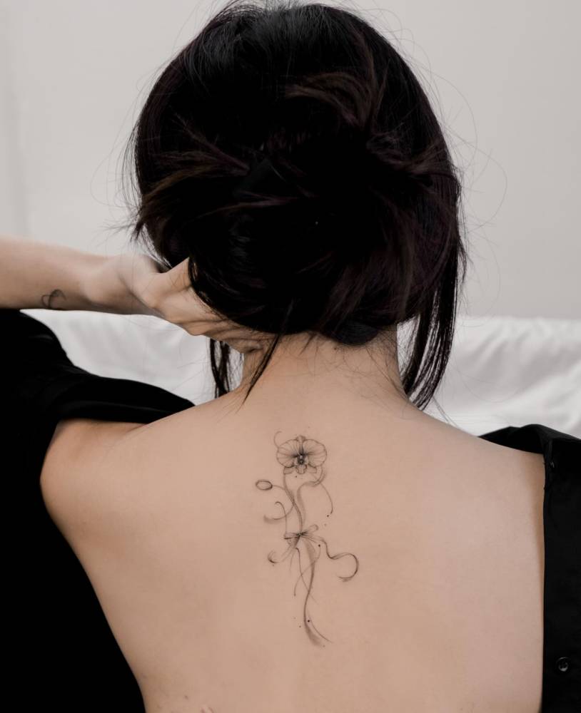 Orchid flower tattooed on the upper back, illustrative style.