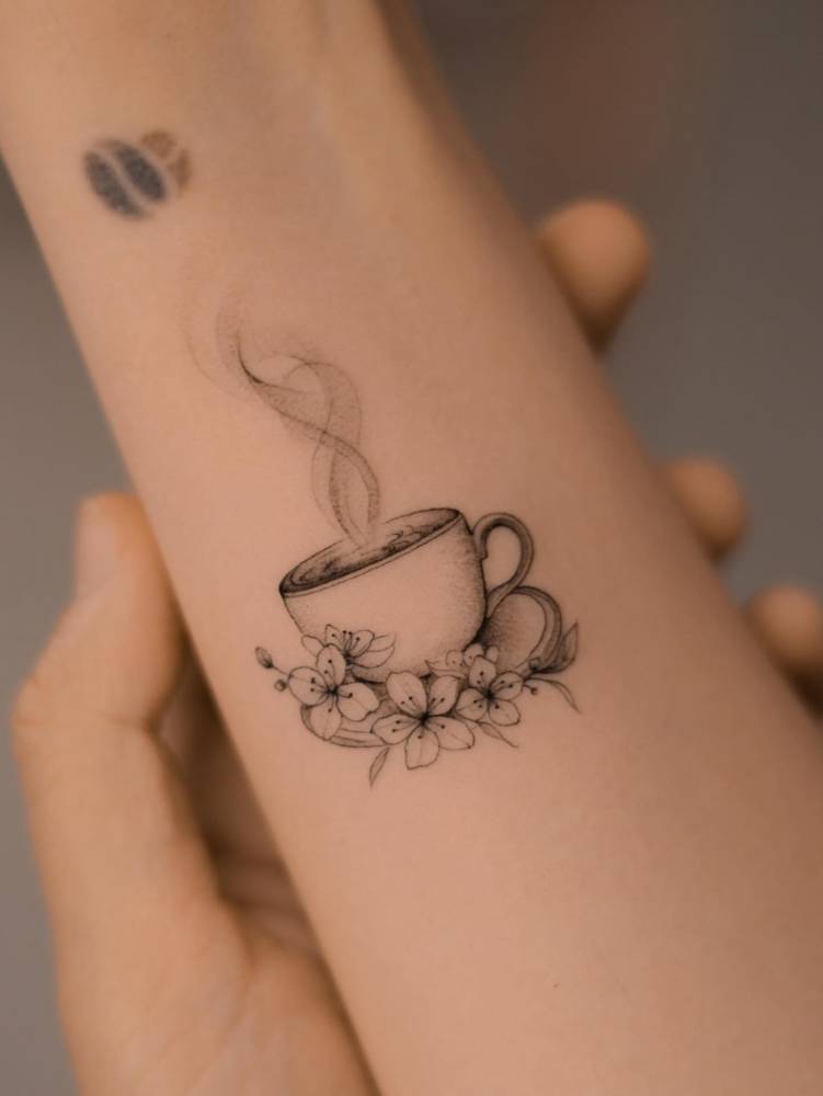 Illustrative style coffee cup tattoo located on the wrist.