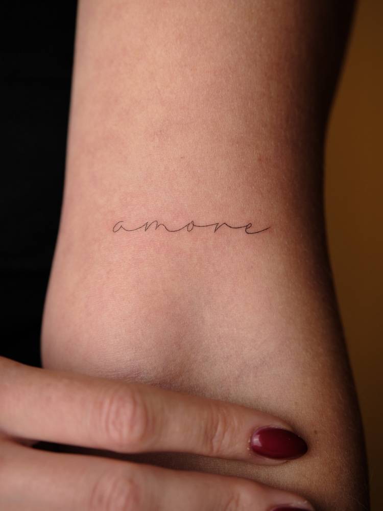 Handwritten font word "amore" tattooed on the bicep.
