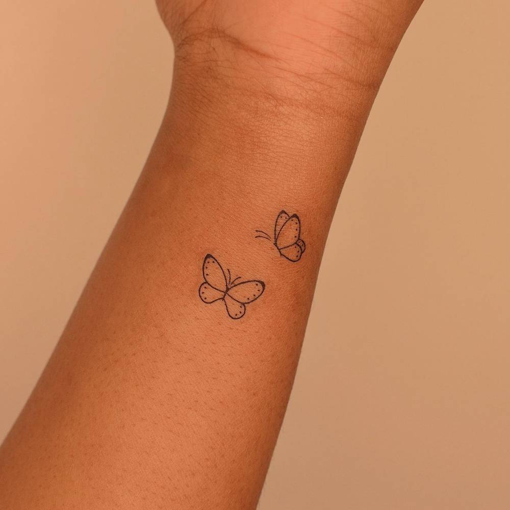 Minimalistic style butterfly couple tattoo located on the wrist.