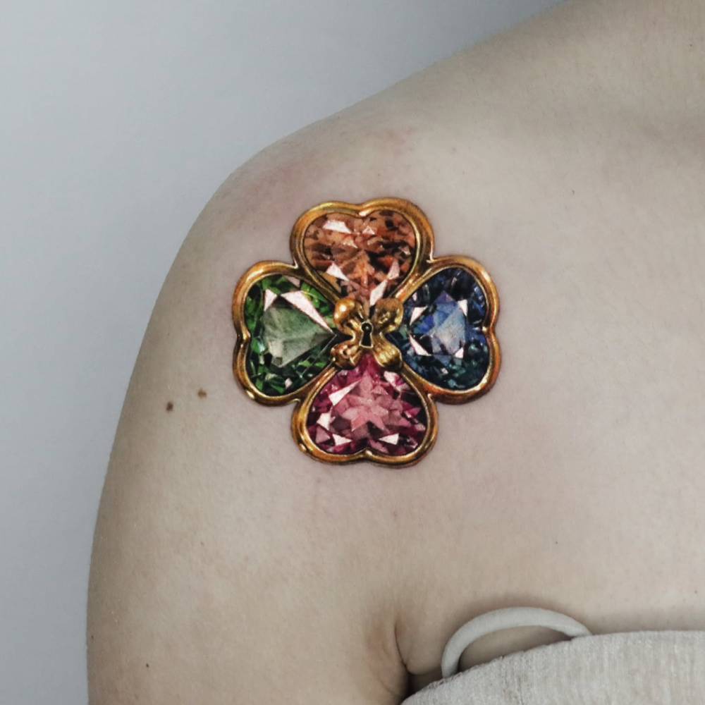 Four leaf clover jewellery tattoo located on the shoulder, micro-realistic style.