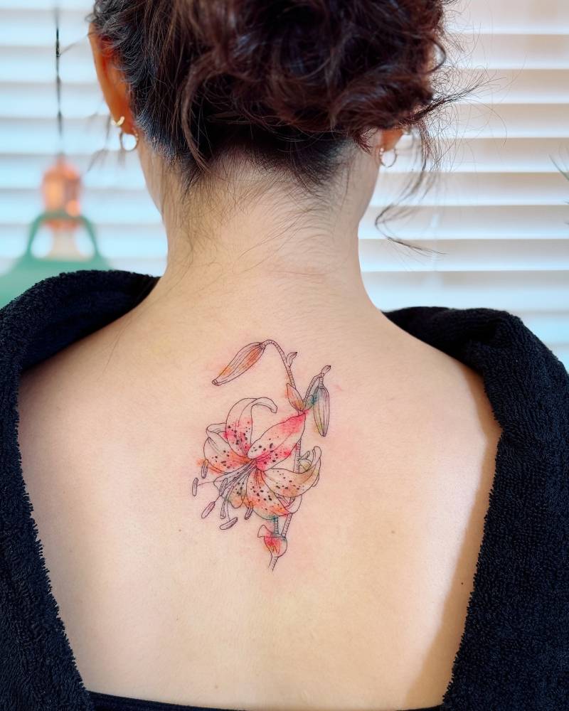 Lily flower tattoo in watercolor style located on the upper back.