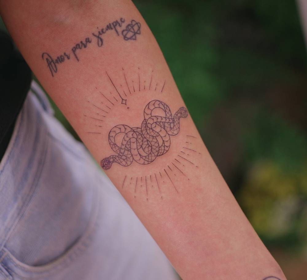 Snake ouroboros tattoo located on the inner forearm, fine line style.