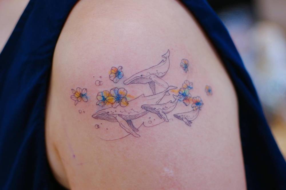 Whale family and flowers tattooed on the upper arm.