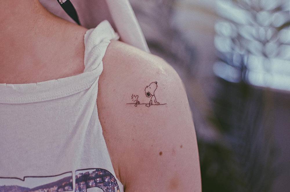 Woodstock and Snoopy tattoo in cartoon style placed on the shoulder.
