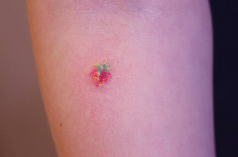 Tiny strawberry tattoo in watercolor style done on the inner forearm.