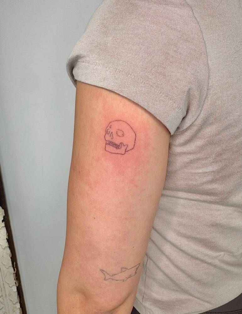 Fine line style skull tattoo located on the tricep.
