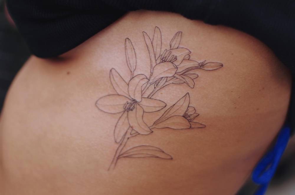 Lily flowers tattooed on the rib, done in fine line style.
