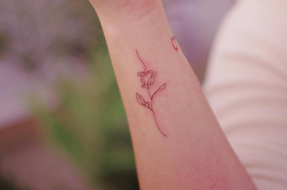 Continuous line rose tattoo located on the wrist.