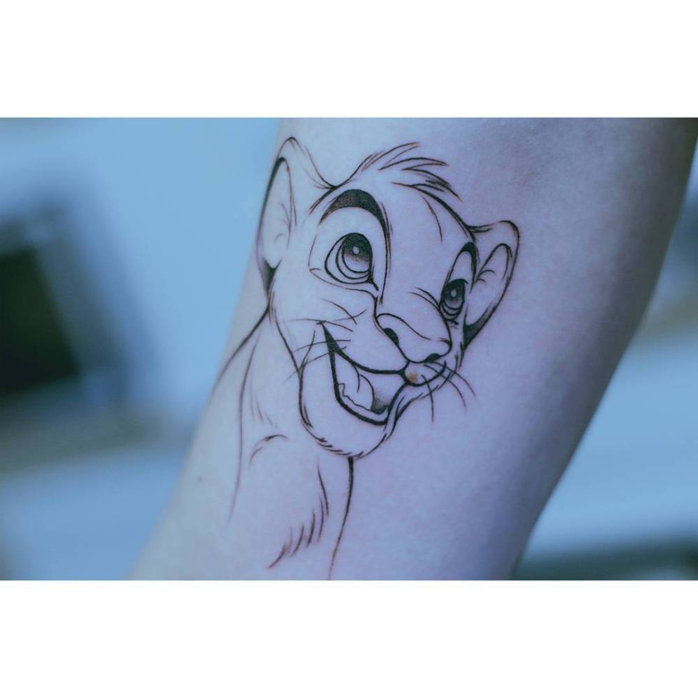 Cartoon style Simba portrait tattoo located on the inner arm.