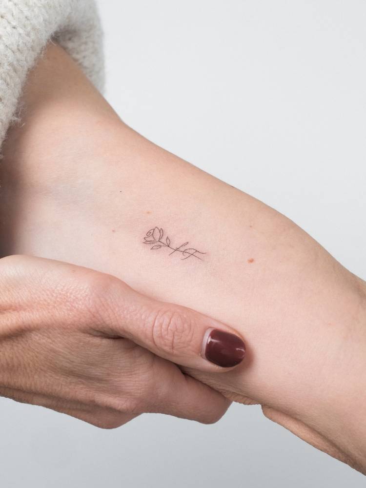 Fine line style rose and initials tattoo located on the inner arm.