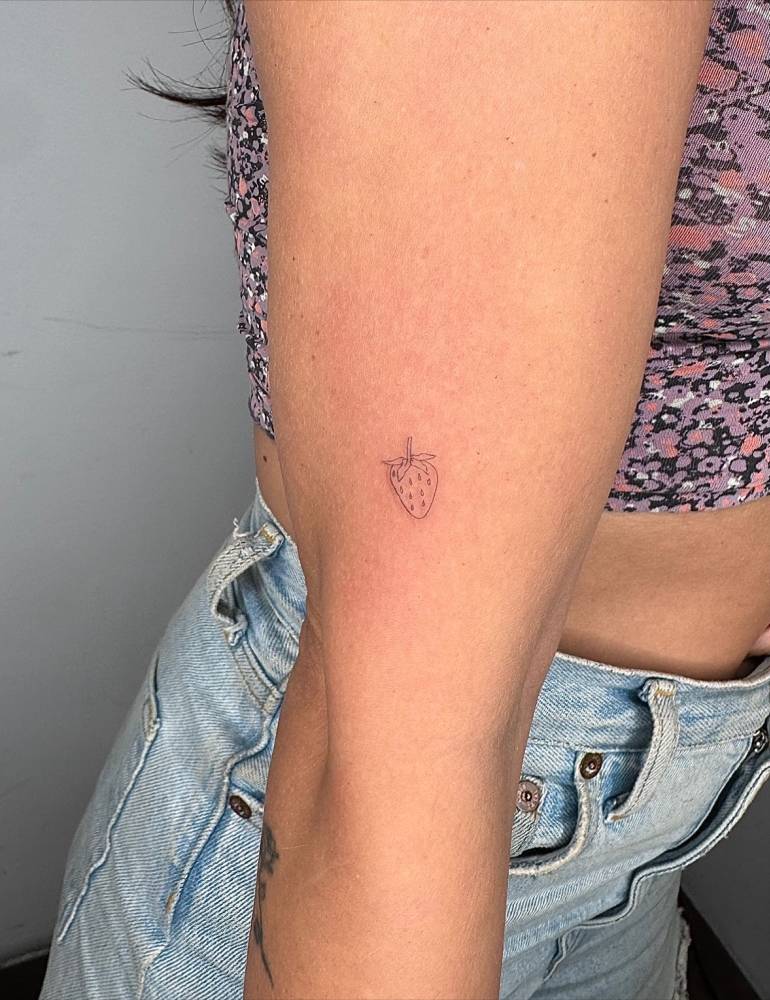 Tiny minimalistic strawberry tattoo located on the upper arm.