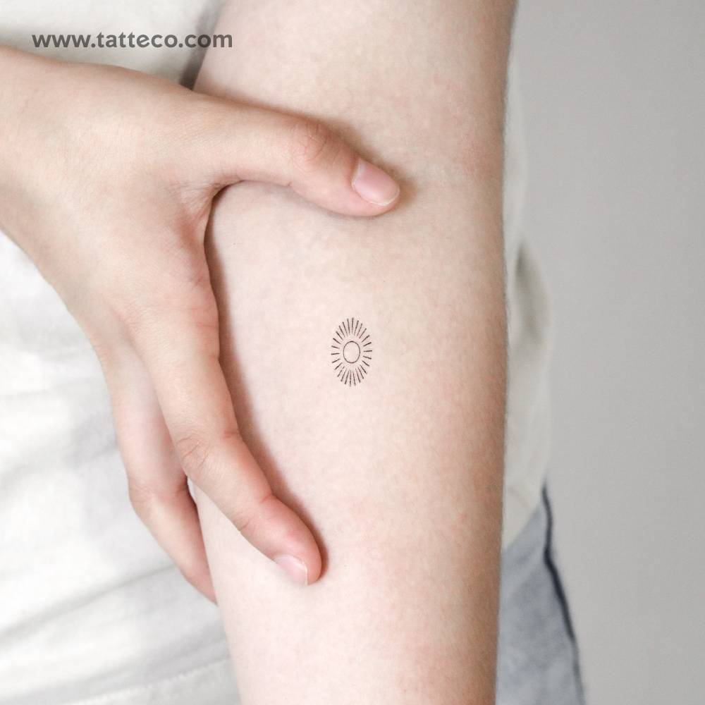 Oval shining sun temporary tattoo located on the inner forearm.