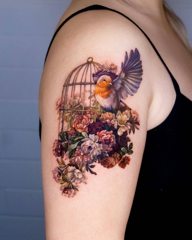 Realistic style robin and bird cage tattoo located on the upper arm.