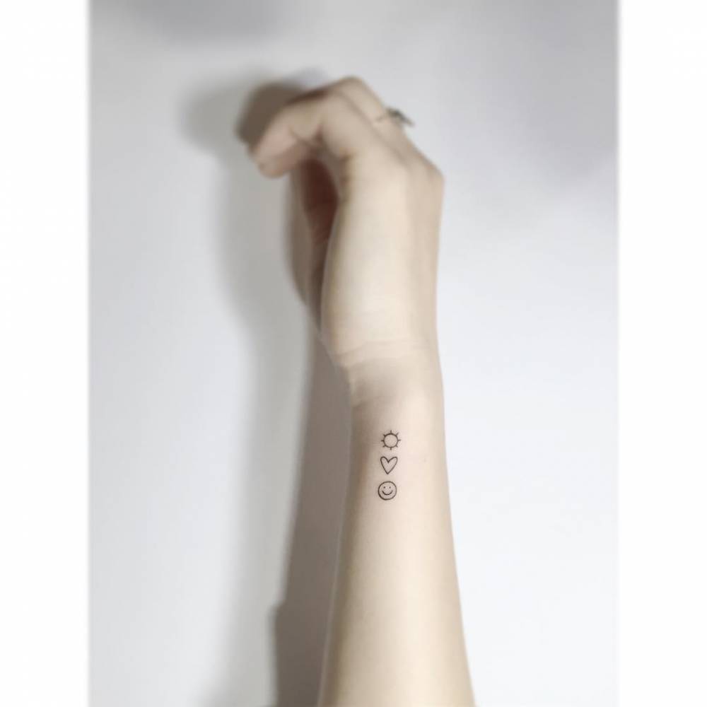 Sun, heart and smiley face tattooed on the wrist, minimalistic style.
