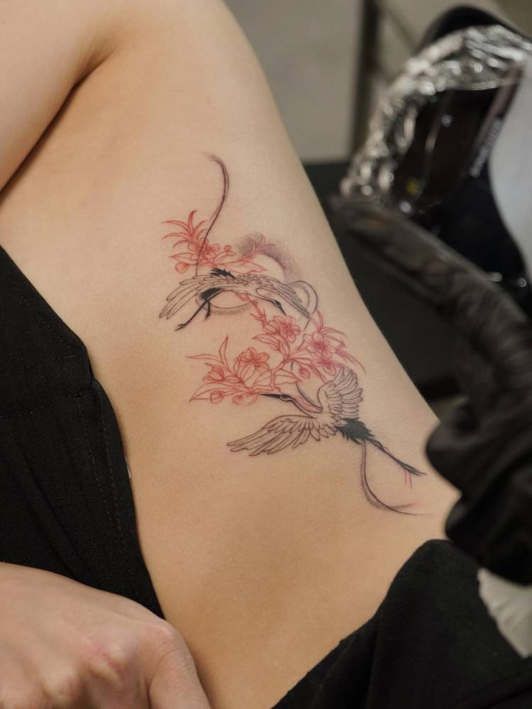 Cranes and cherry blossoms tattooed on the rib, illustrative style.