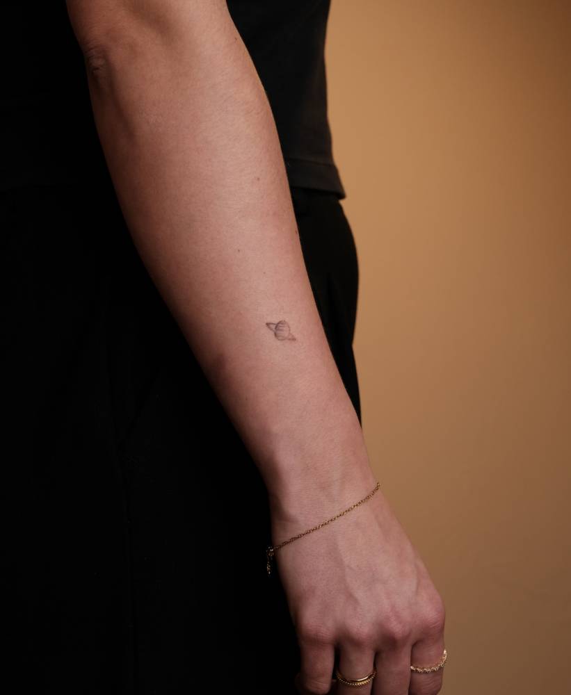 Tiny Saturn tattoo located on the wrist.