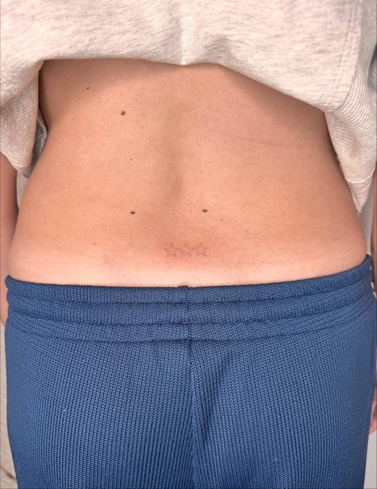 Three stars in minimalistic style tattooed on the lower back.