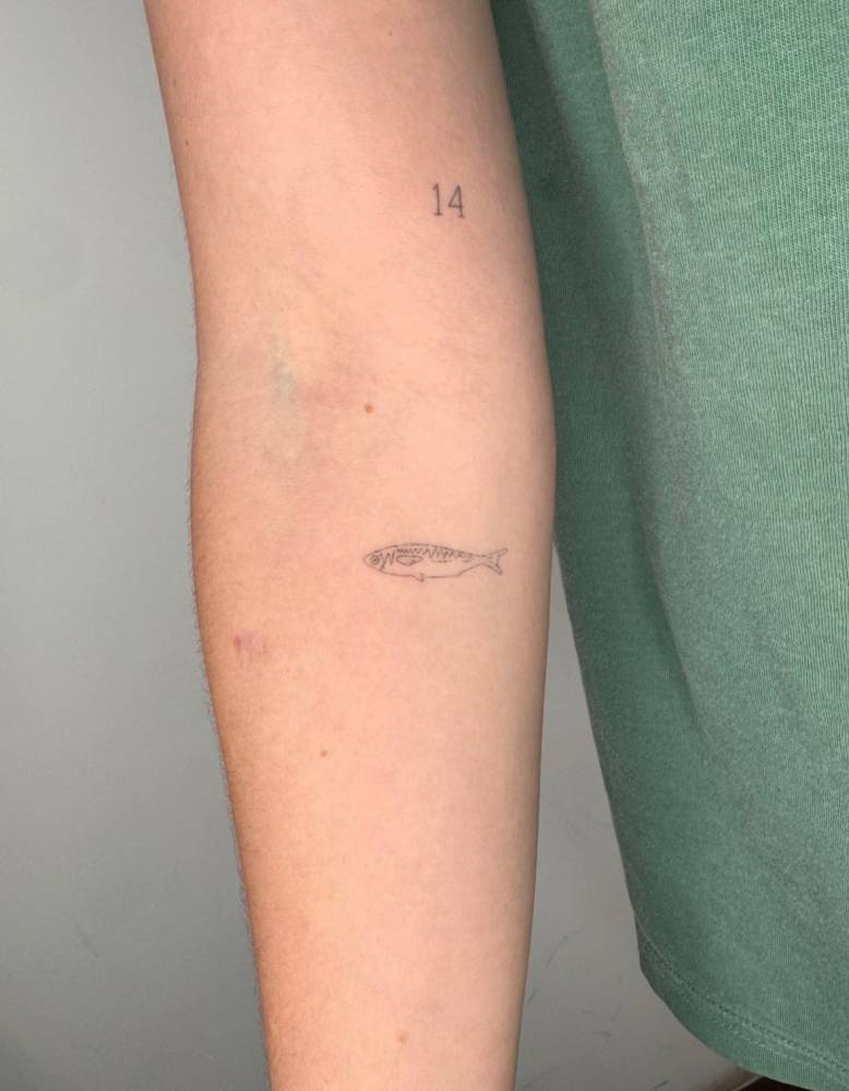 Healed sardine tattoo in fine line style located on the inner forearm.