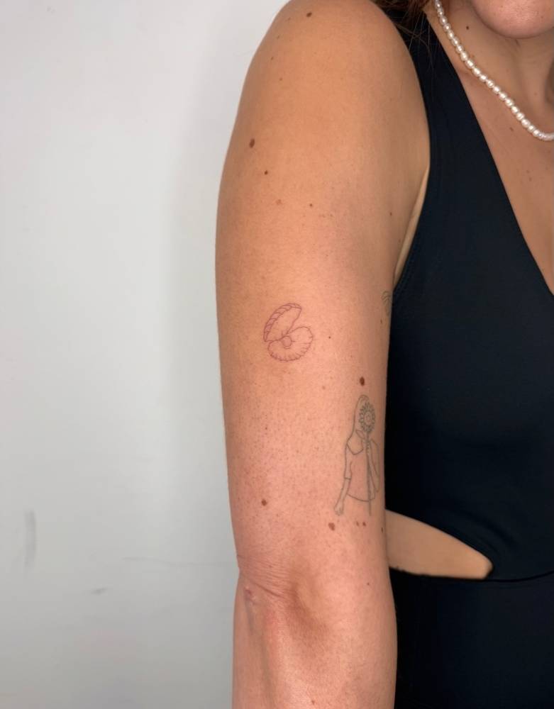 Scallop tattoo in fine line style located on the upper arm.