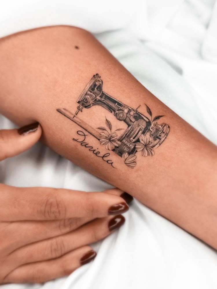 Sewing machine tattoo located on the inner forearm, micro-realistic style.