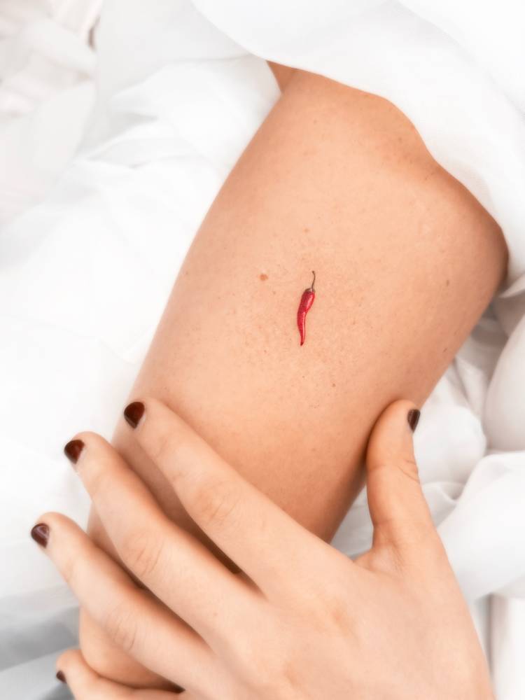 Tiny red chili tattoo in micro-realistic style located on the tricep.