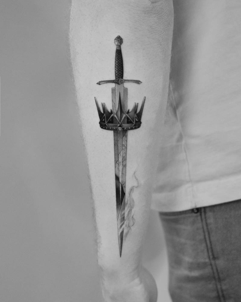 Micro-realistic style sword and crown tattoo placed on the forearm.
