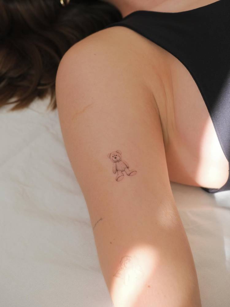 Single needle teddy bear tattoo located on the bicep.