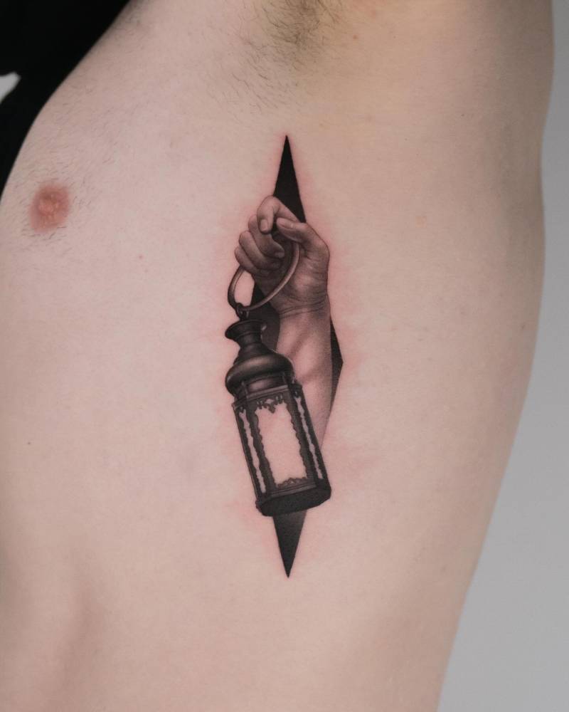 Hand holding a lantern tattooed on the rib.