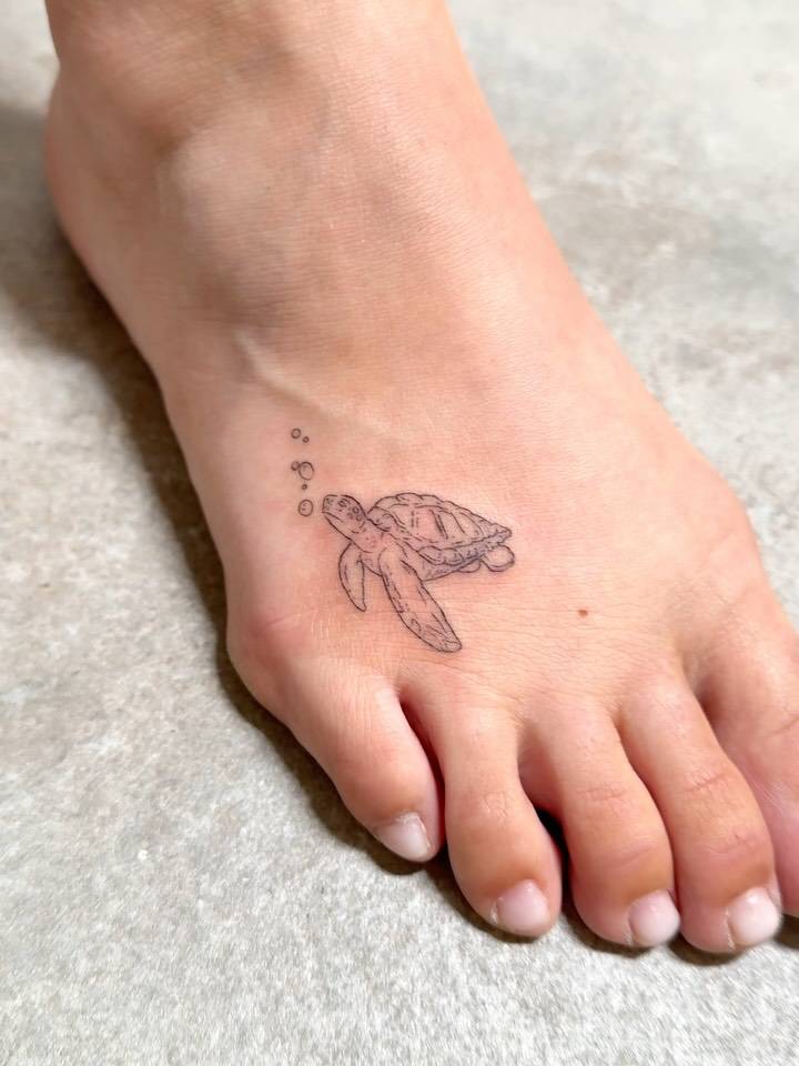 Turtle tattoo located on the foot, done in fine line style.