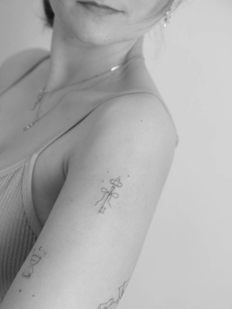 Single needle key and bow tattoo located on the upper arm.