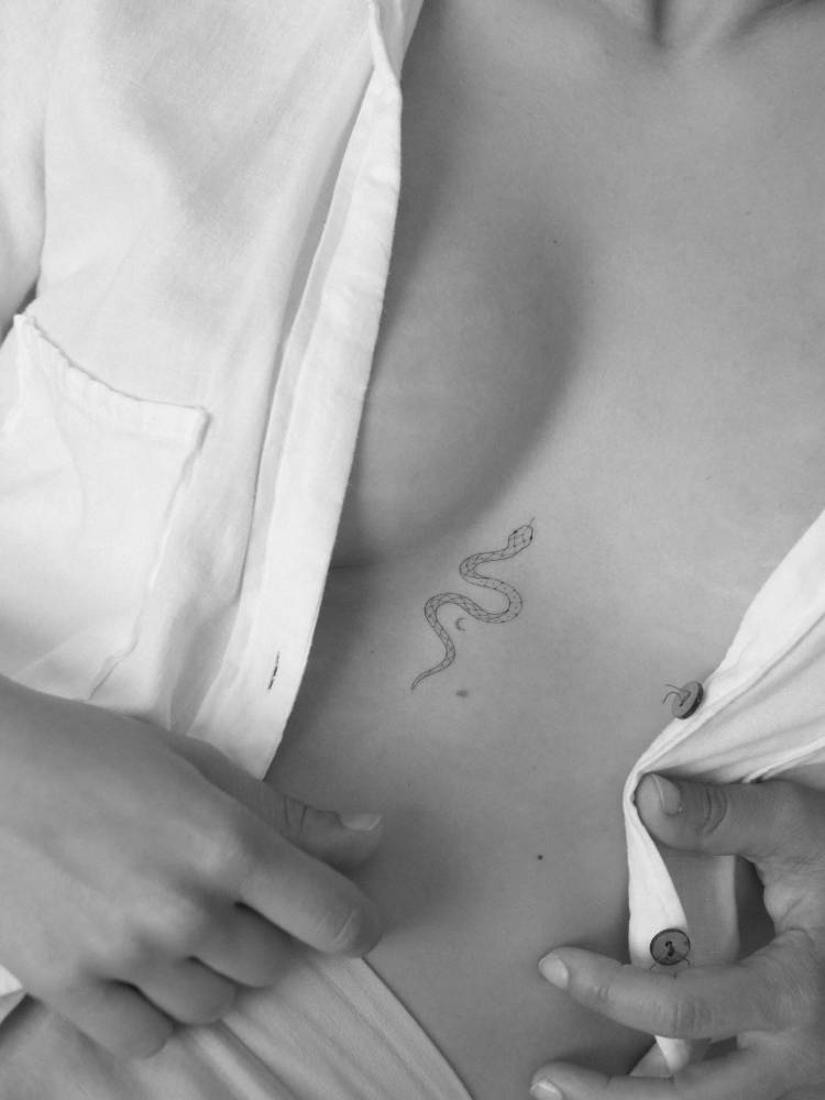 Little snake in fine line style tattooed on the sternum.