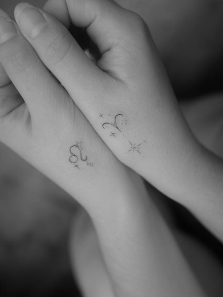 Individual matching Leo and Aries zodiac symbols tattooed on the hands.